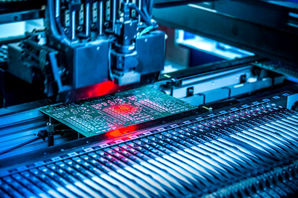 Circuit board being manufactured by an automated assembly machine, illuminated with blue and red lights.