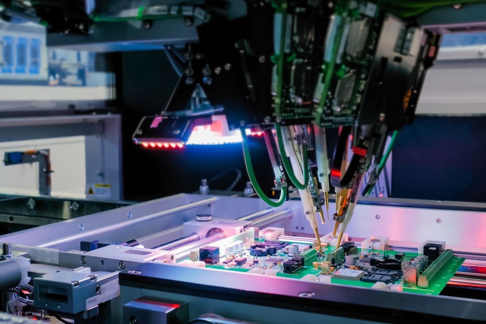 Robotic arm assembling a circuit board, industrial setting with blue and red lights.
