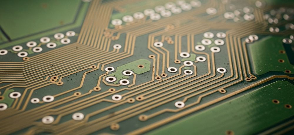 Close-up of a green circuit board with gold-colored wiring and components.