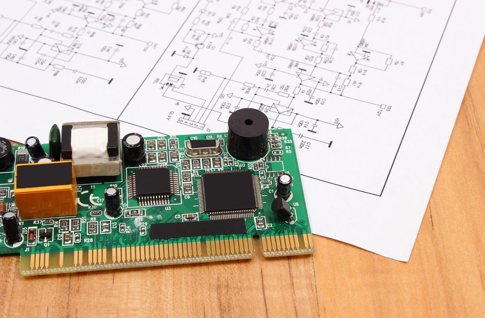 Green circuit board on a wooden desk with technical schematics in the background