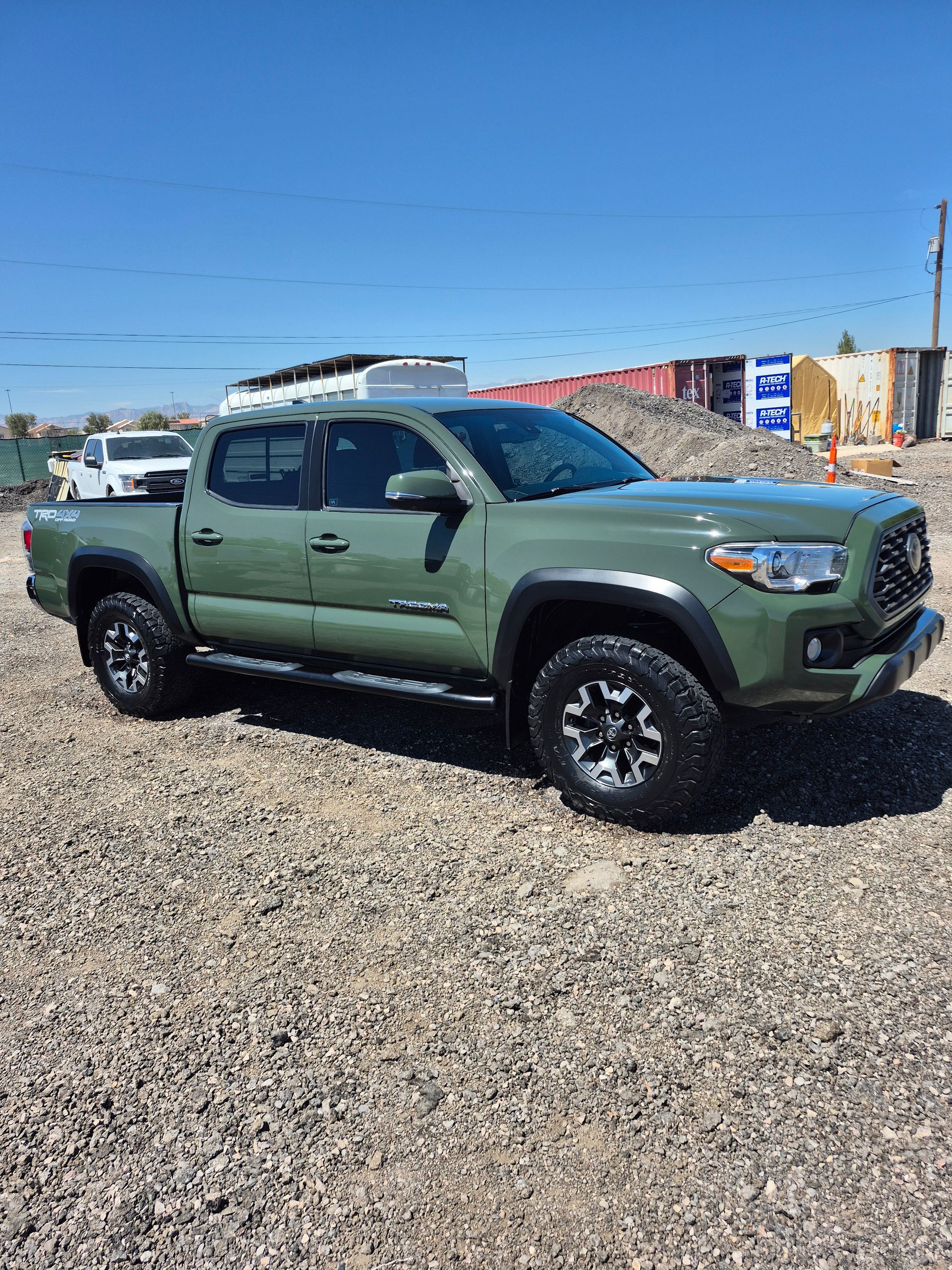 Green pickup truck parked on gravel under a clear blue sky