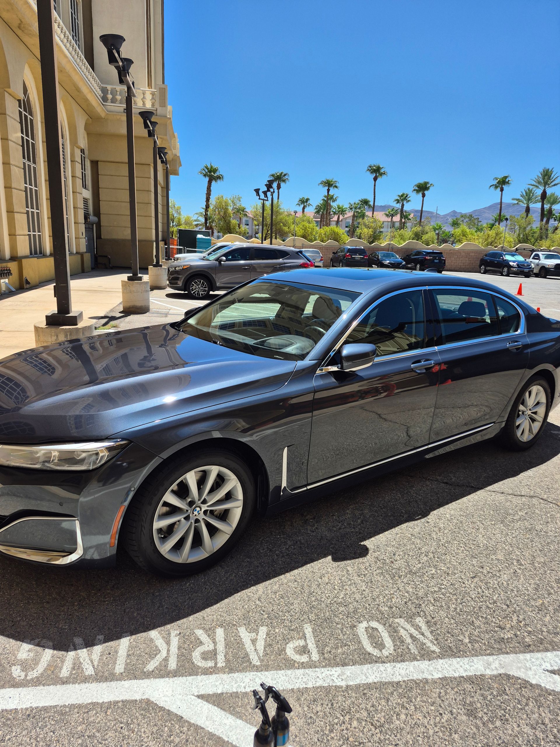 Black sedan parked by a hotel entrance on a sunny street with palm trees and mountains in the distance