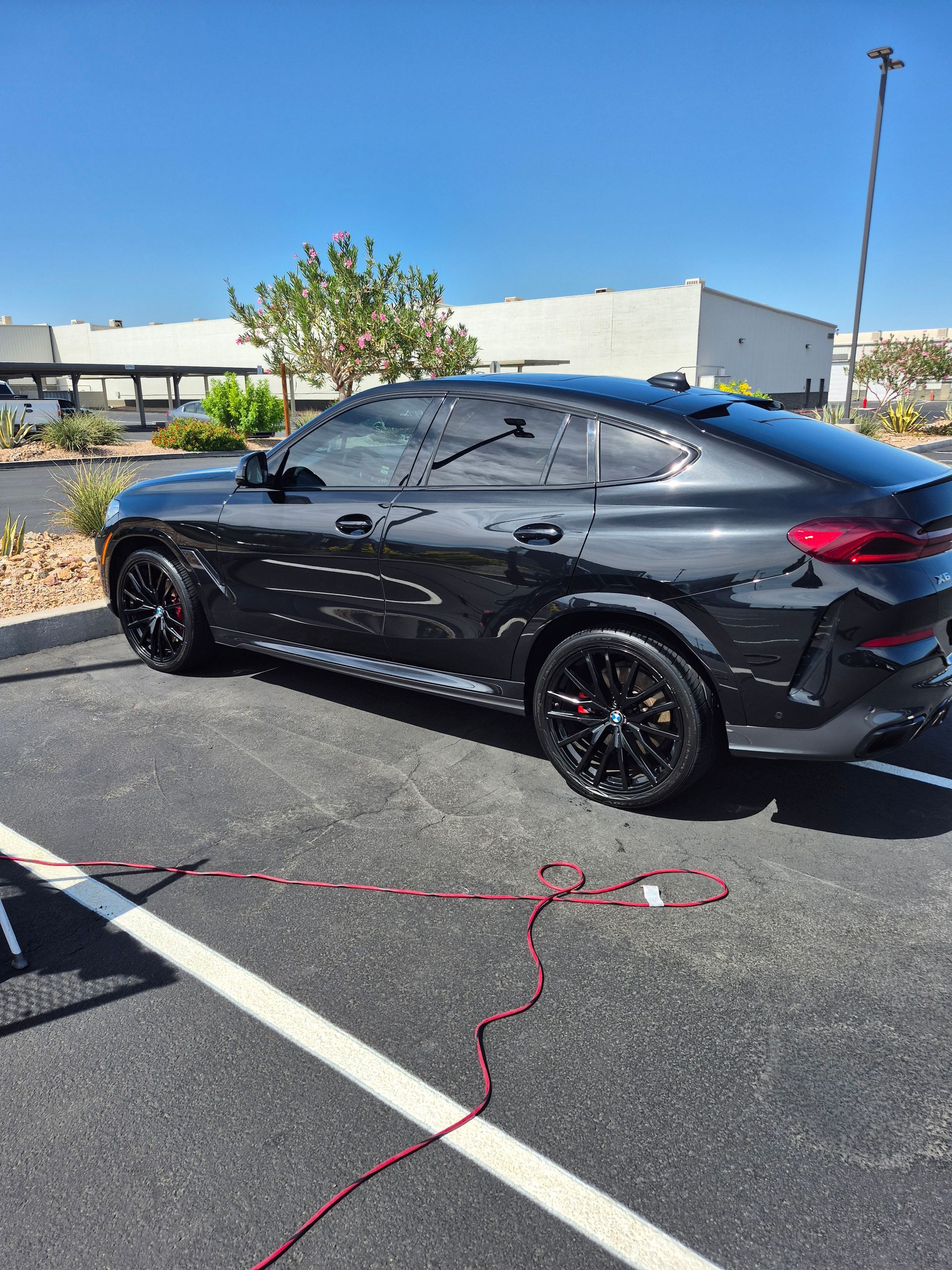 Black SUV parked in a lot beside a charging cable, with trees and buildings in the background