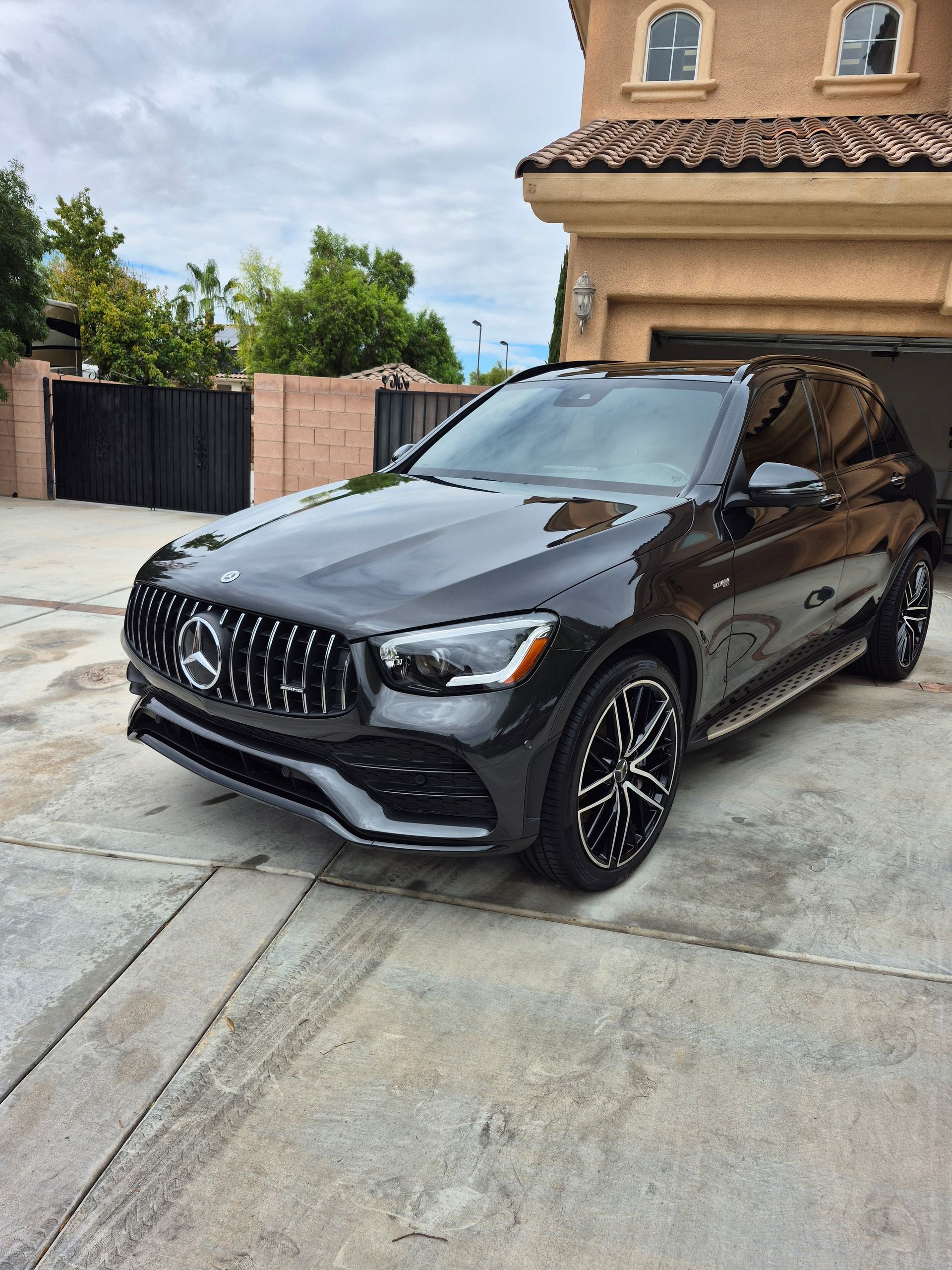 Black Mercedes-Benz SUV parked in a driveway beside a beige house.