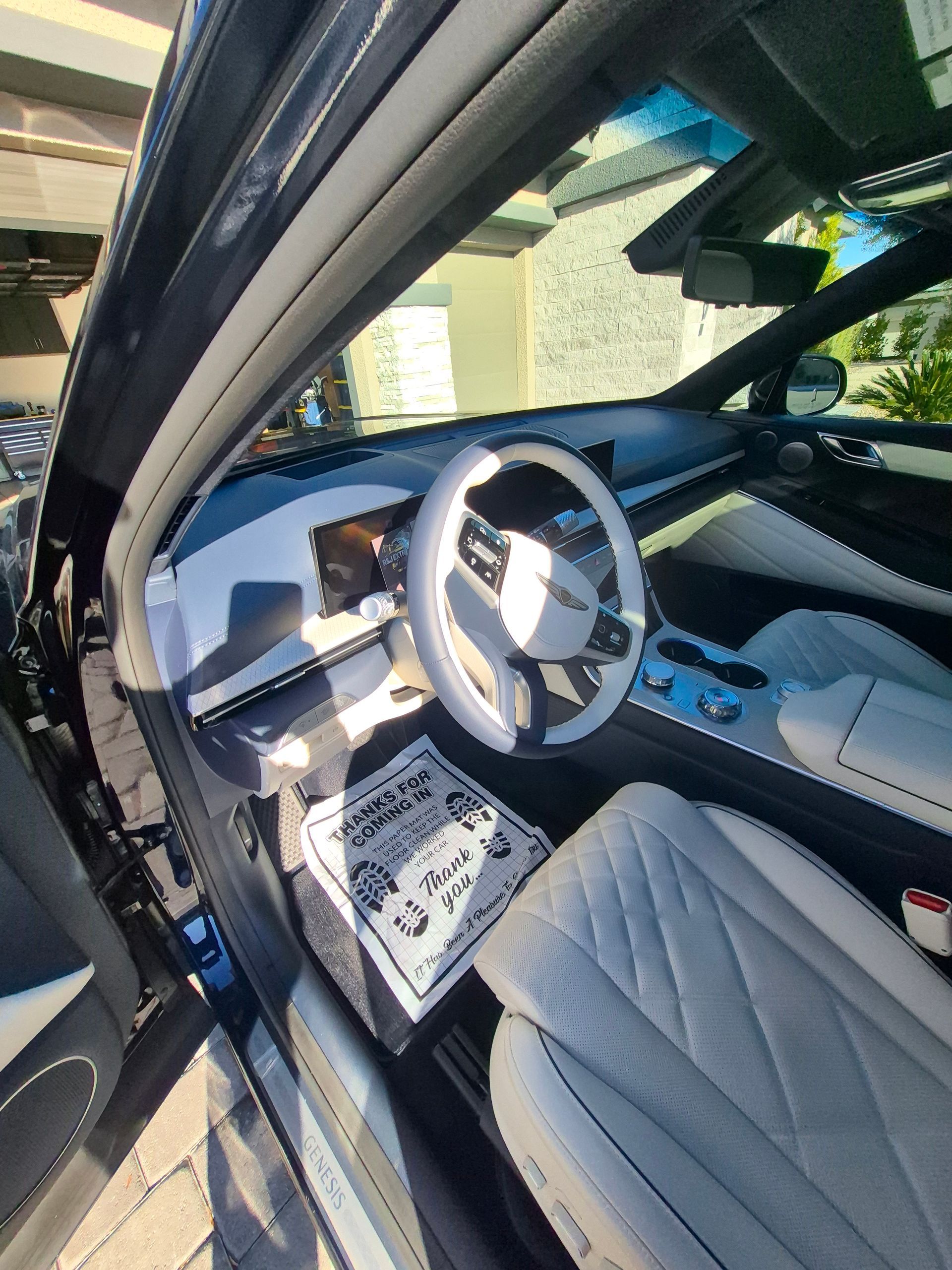 Car interior with white quilted seats and steering wheel, viewed through an open door in sunlight