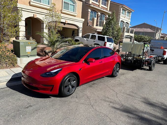 Red Tesla Model 3 parked on street in front of a house.