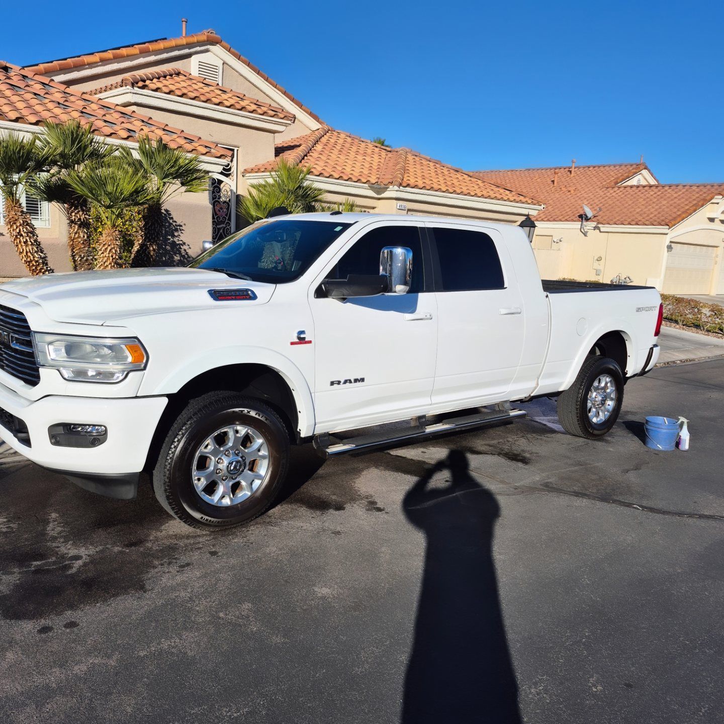 White pickup truck parked in a driveway beside a stucco house under a clear blue sky