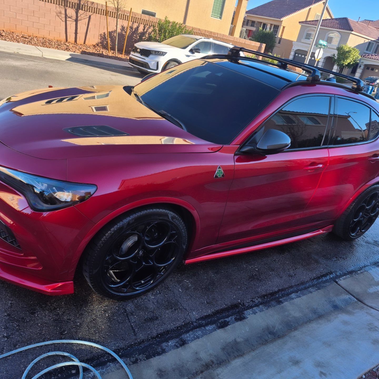 Red sports coupe with black wheels parked on a driveway in a suburban neighborhood.