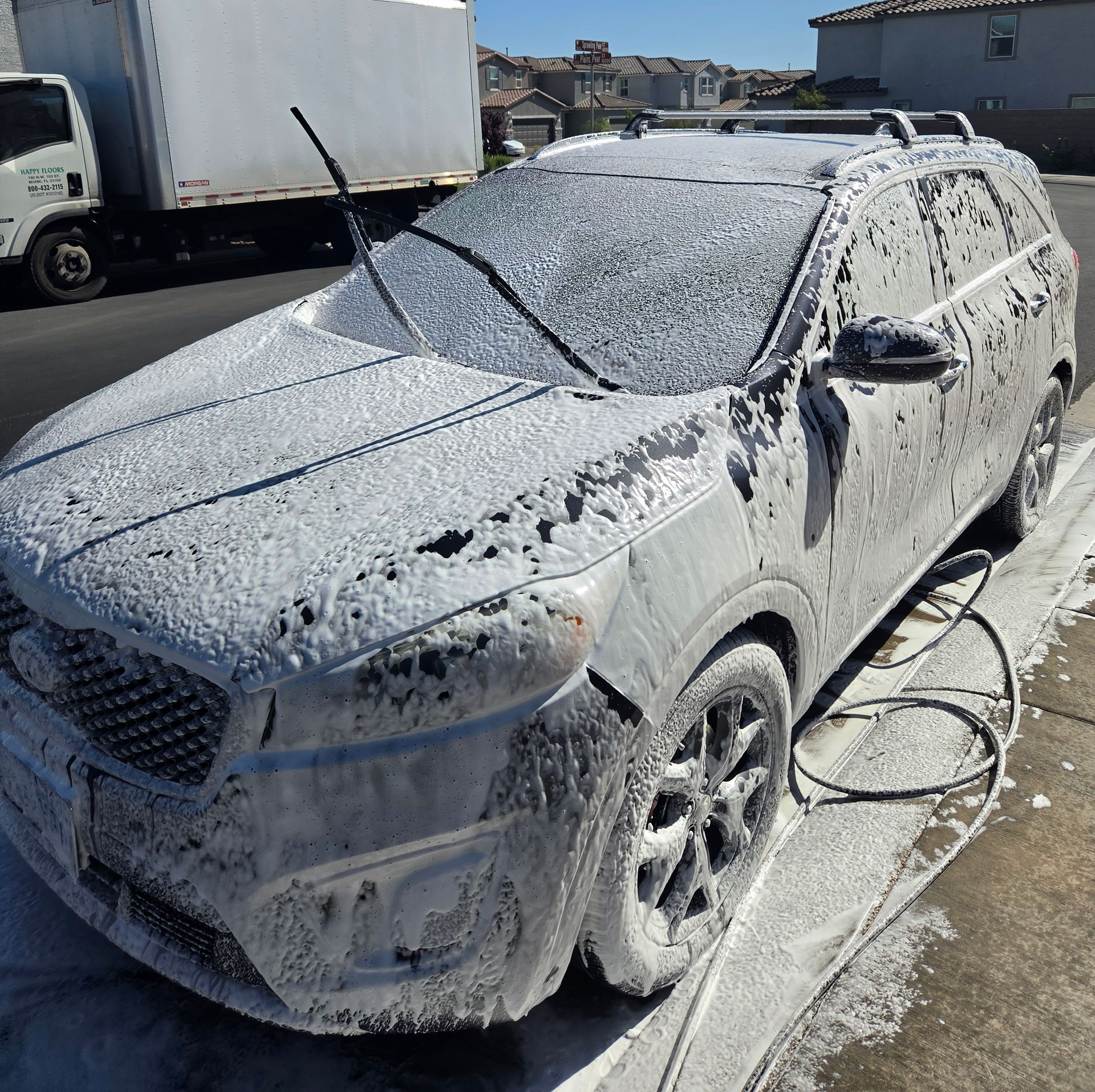 Silver SUV covered in white foam at a car wash, with hose on the ground