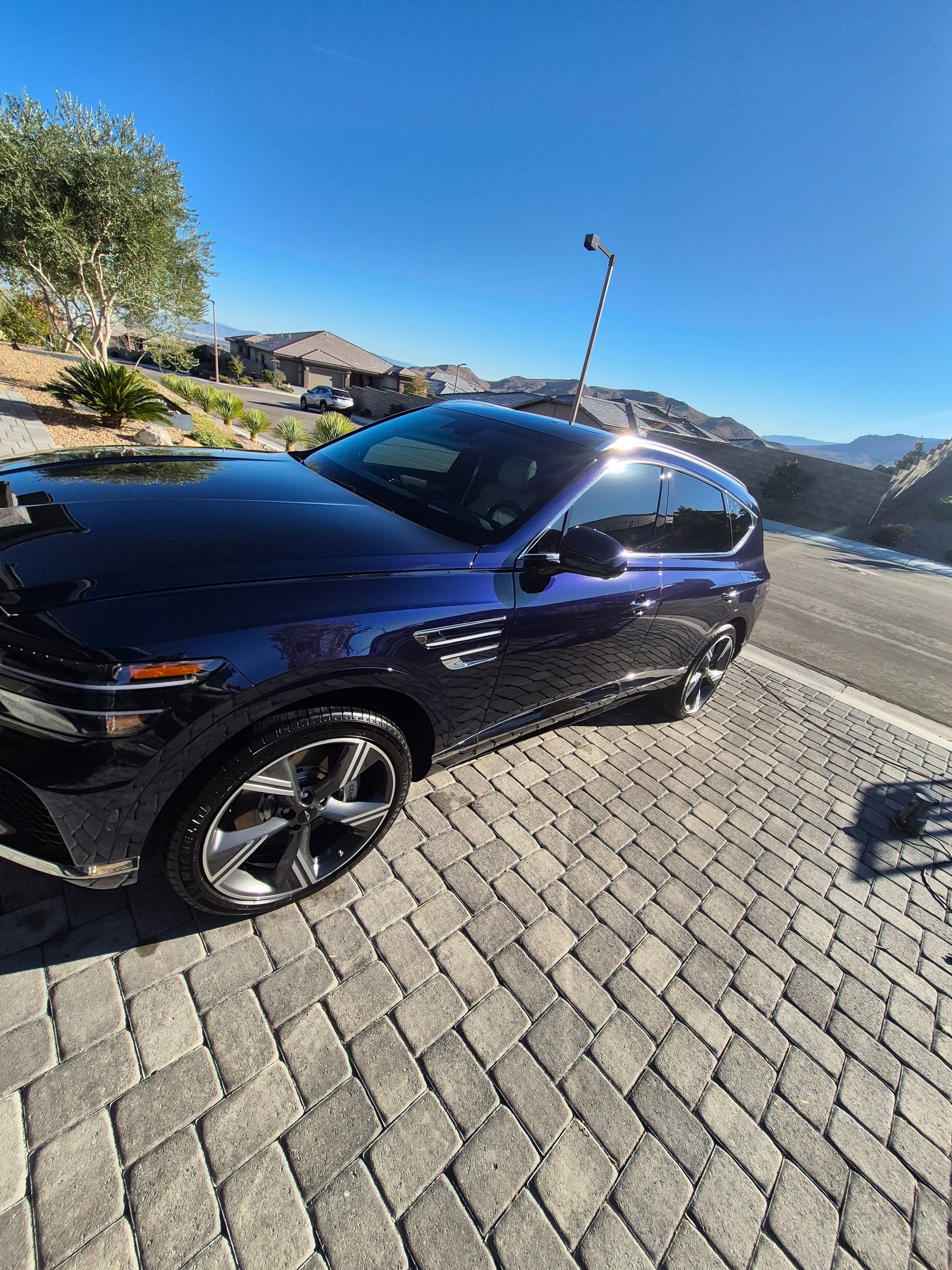 Black SUV parked on a sunlit cobblestone street with mountains in the background