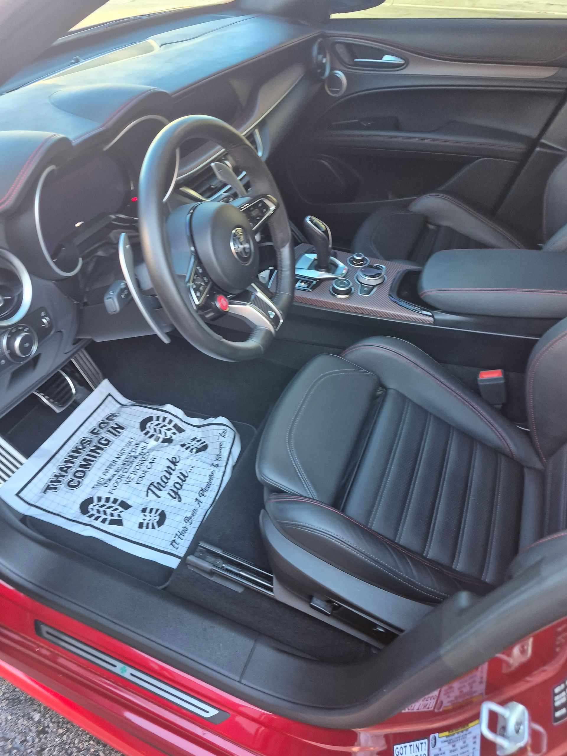 Red sports car interior with black seats, steering wheel, center console, and a floor mat on the driver's side