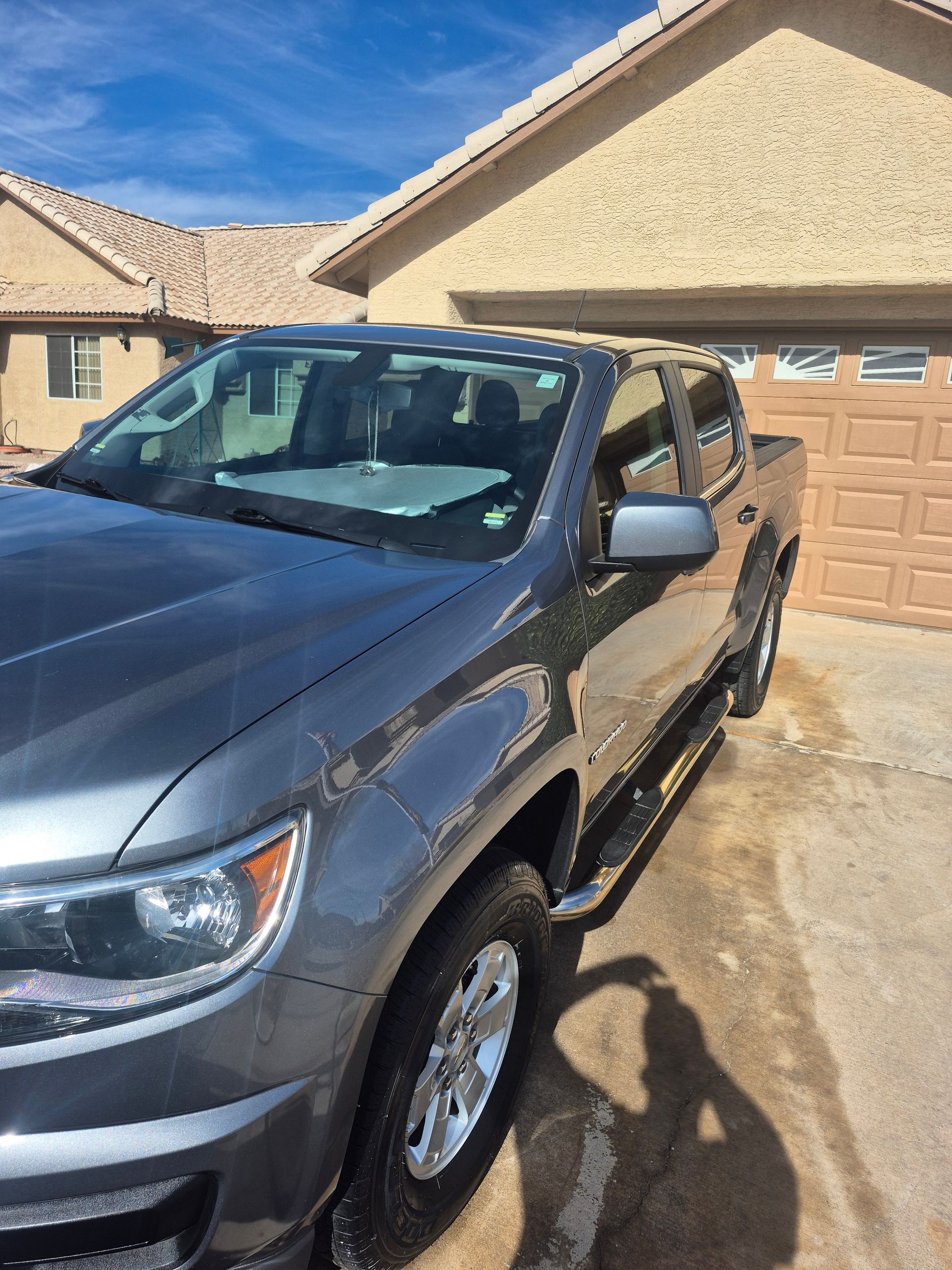 Dark gray pickup truck parked in a driveway in front of a tan garage under a blue sky