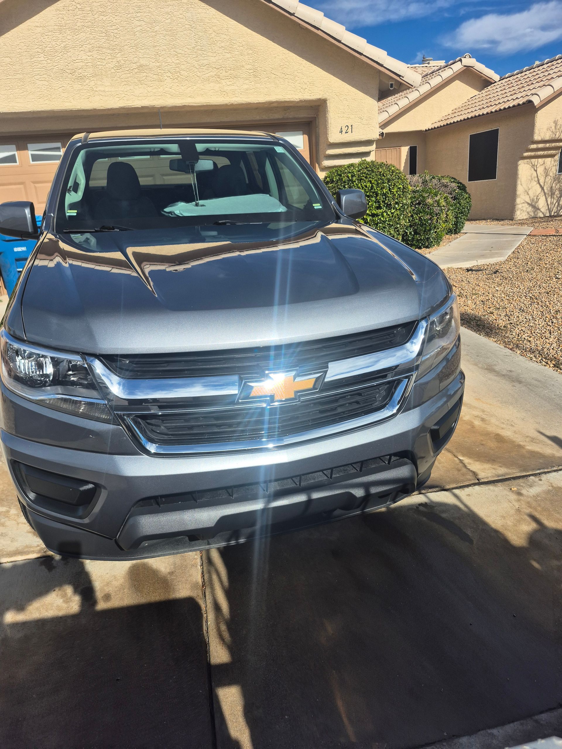 Gray Chevrolet SUV parked in a sunlit driveway outside a beige house.