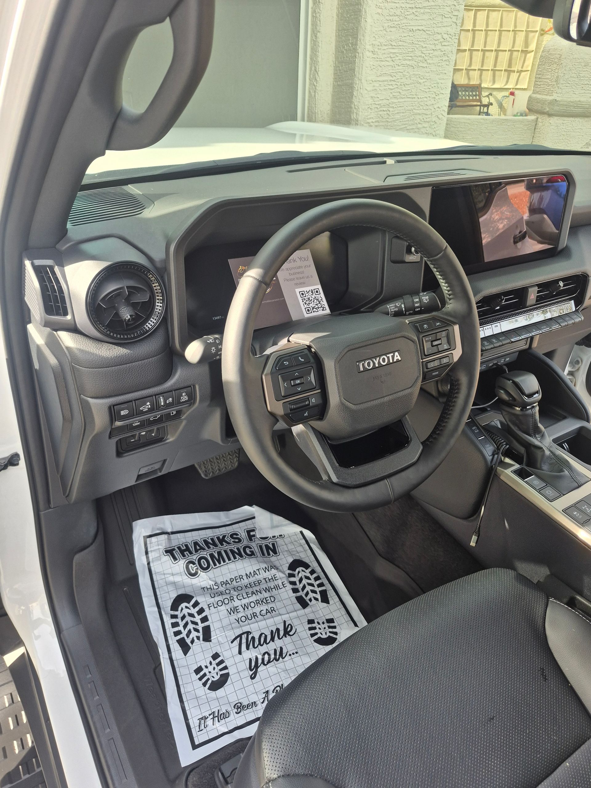 Truck cab interior with steering wheel, dashboard screen, and a paper floor mat on the driver's seat area