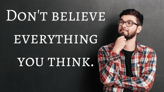 A man in a plaid shirt is standing in front of a blackboard with the words don't believe everything you think.