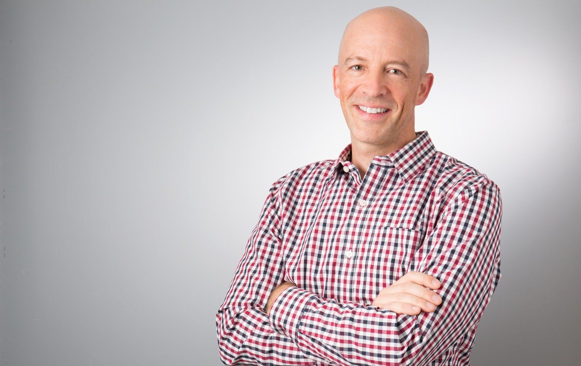 Michael Ceely in a plaid shirt smiles with arms crossed.