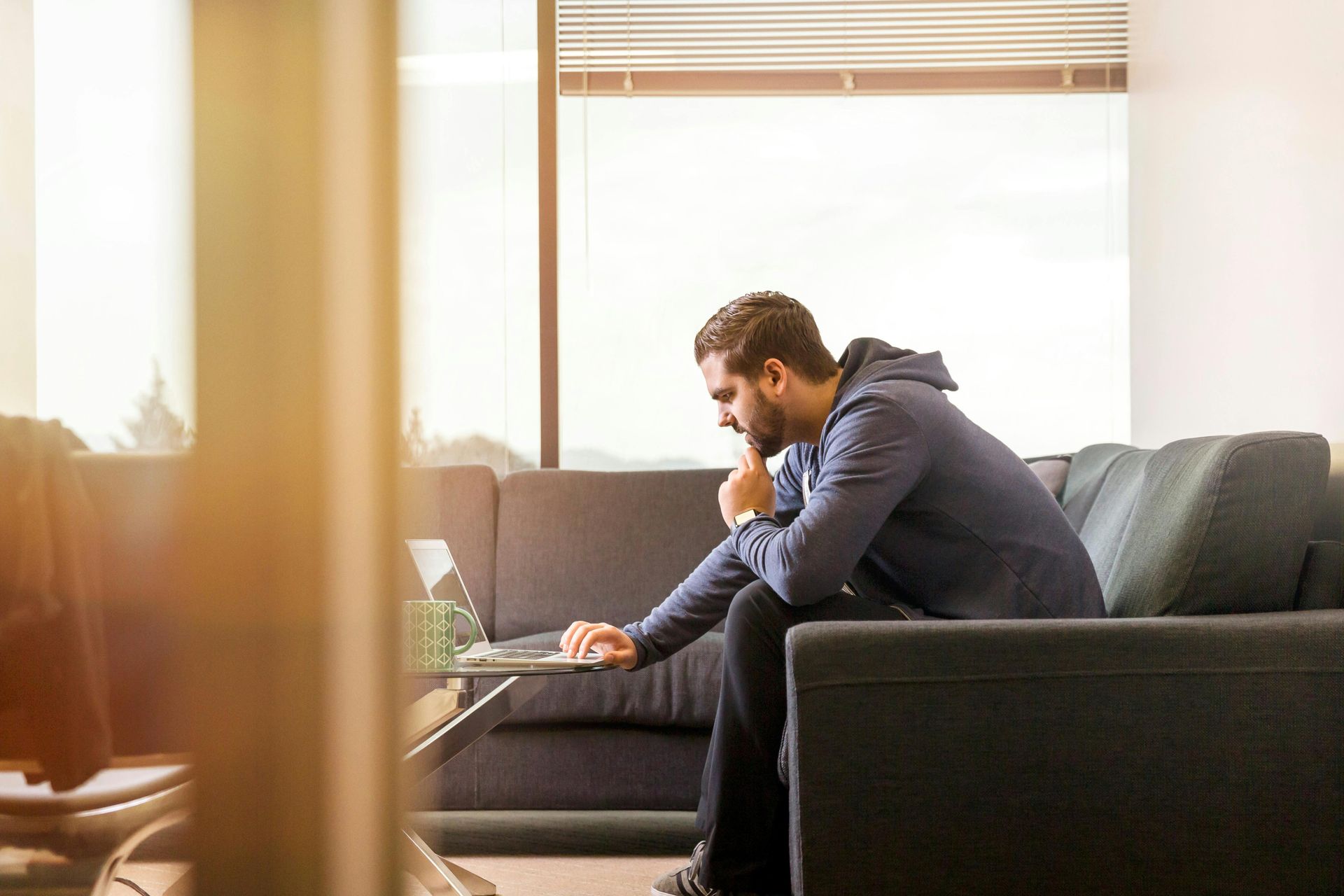 A man is sitting on a couch using a laptop computer.