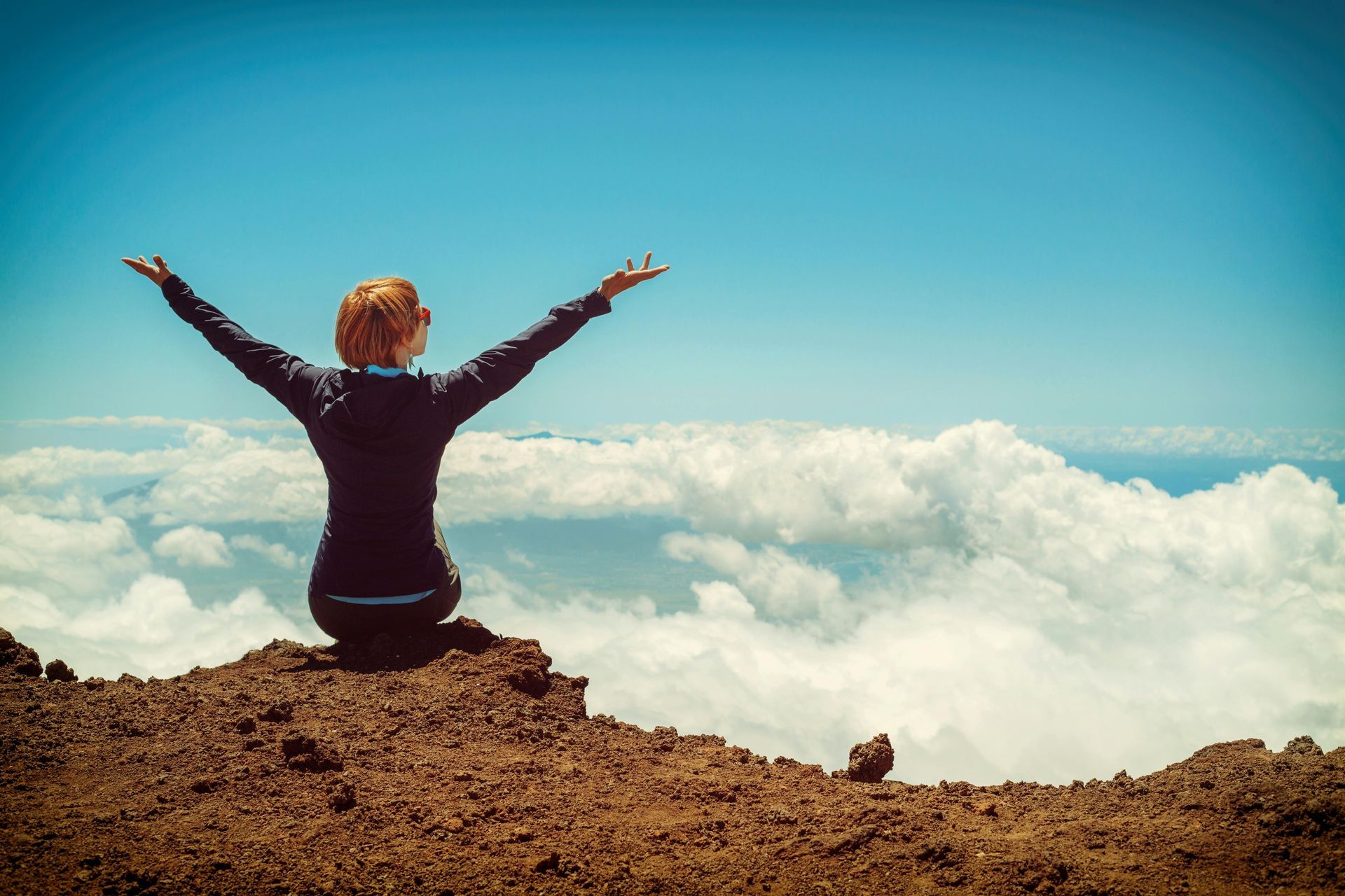A woman is sitting on top of a mountain with her arms outstretched.