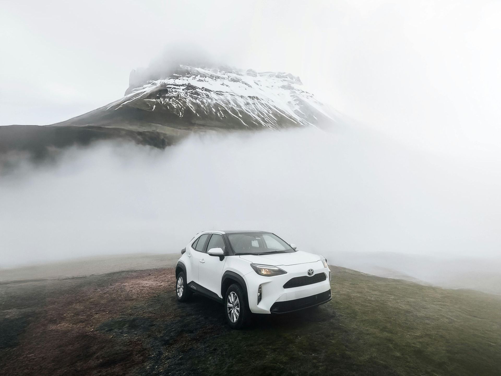 A white car is parked on top of a mountain in the fog.