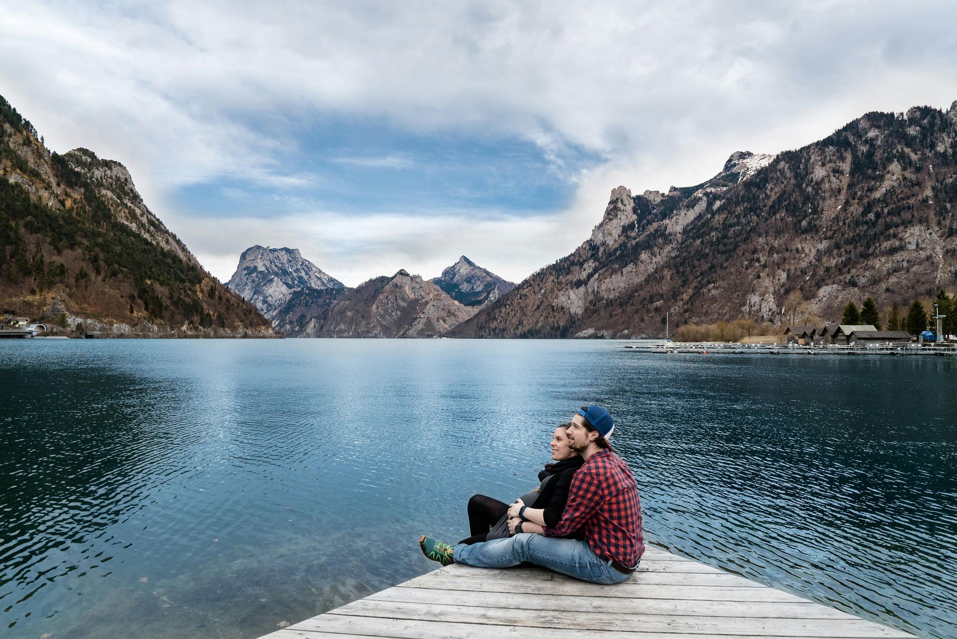 A man and a woman are sitting on a dock overlooking a lake.