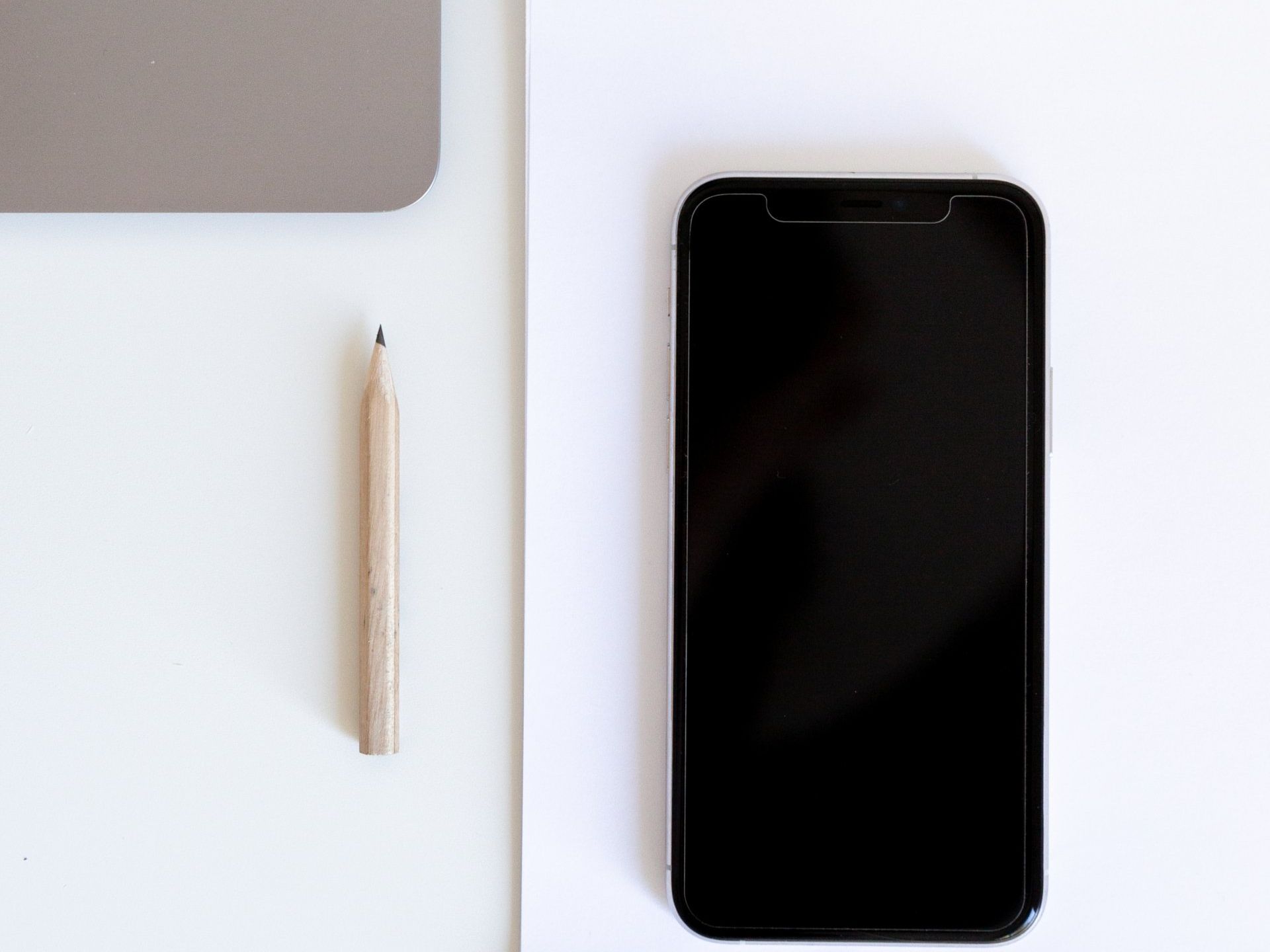 Cell phone on a white table next to a pencil.