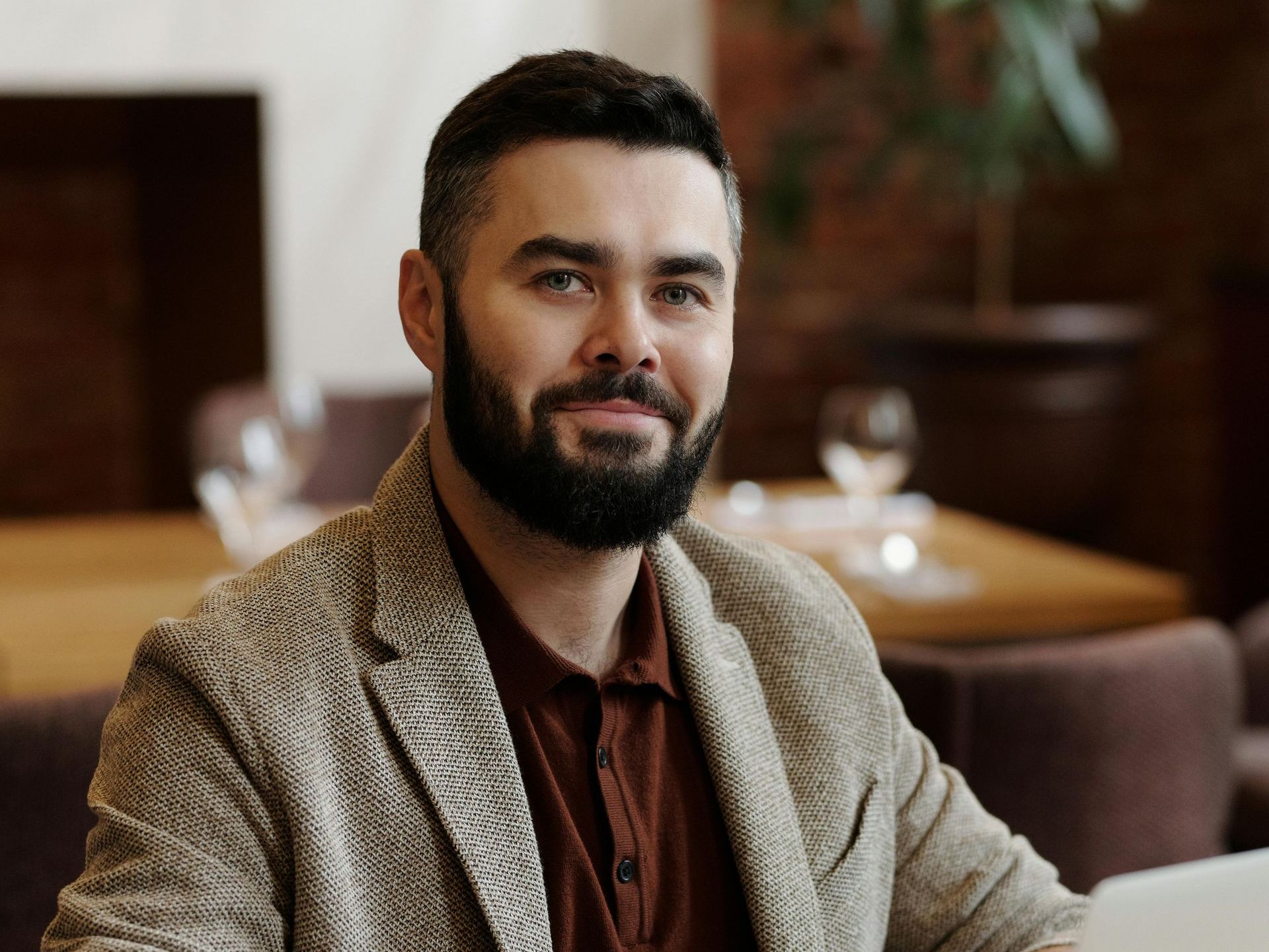A man with a beard is sitting at a table with a laptop.