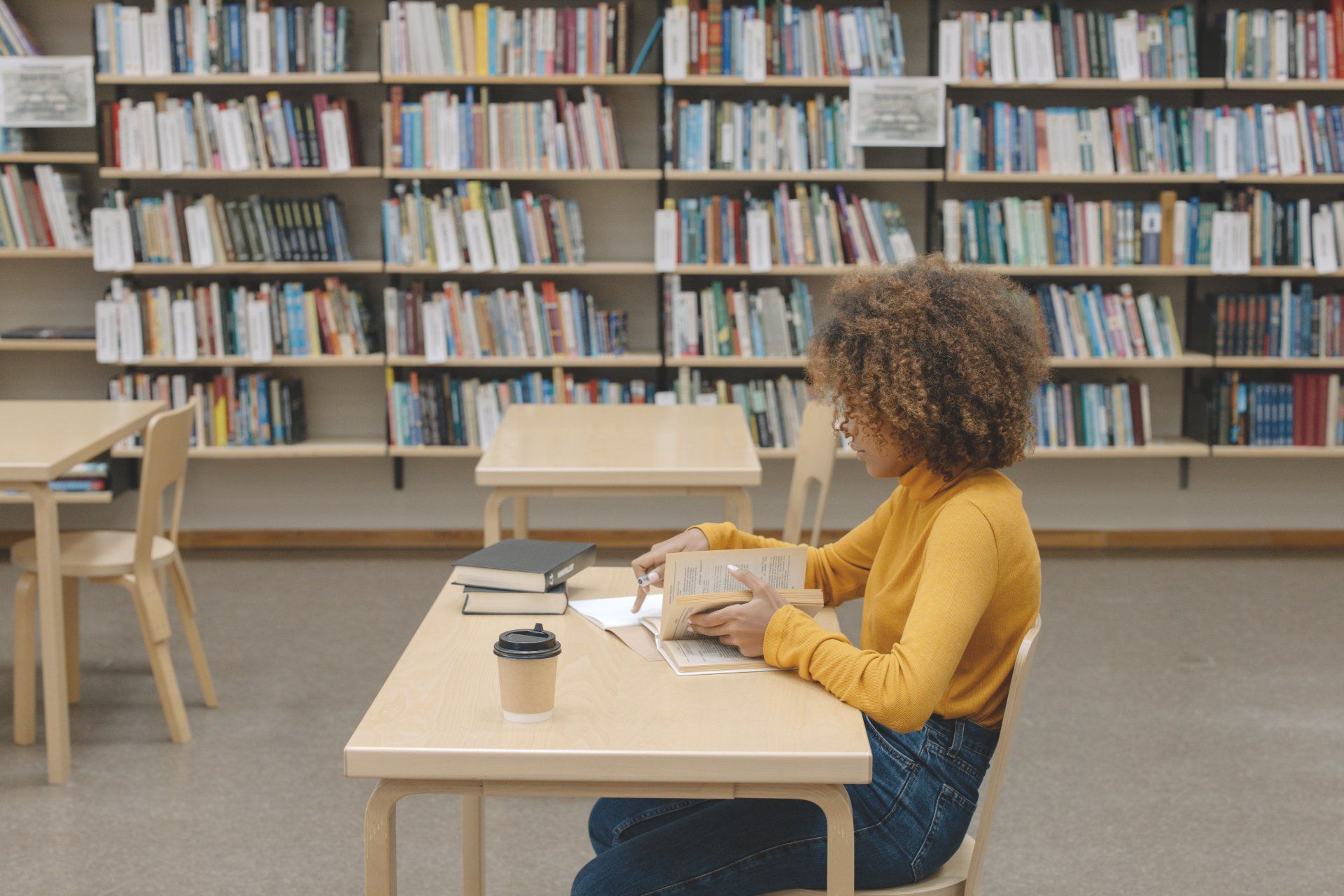 A woman is sitting at a desk in a library reading a book.