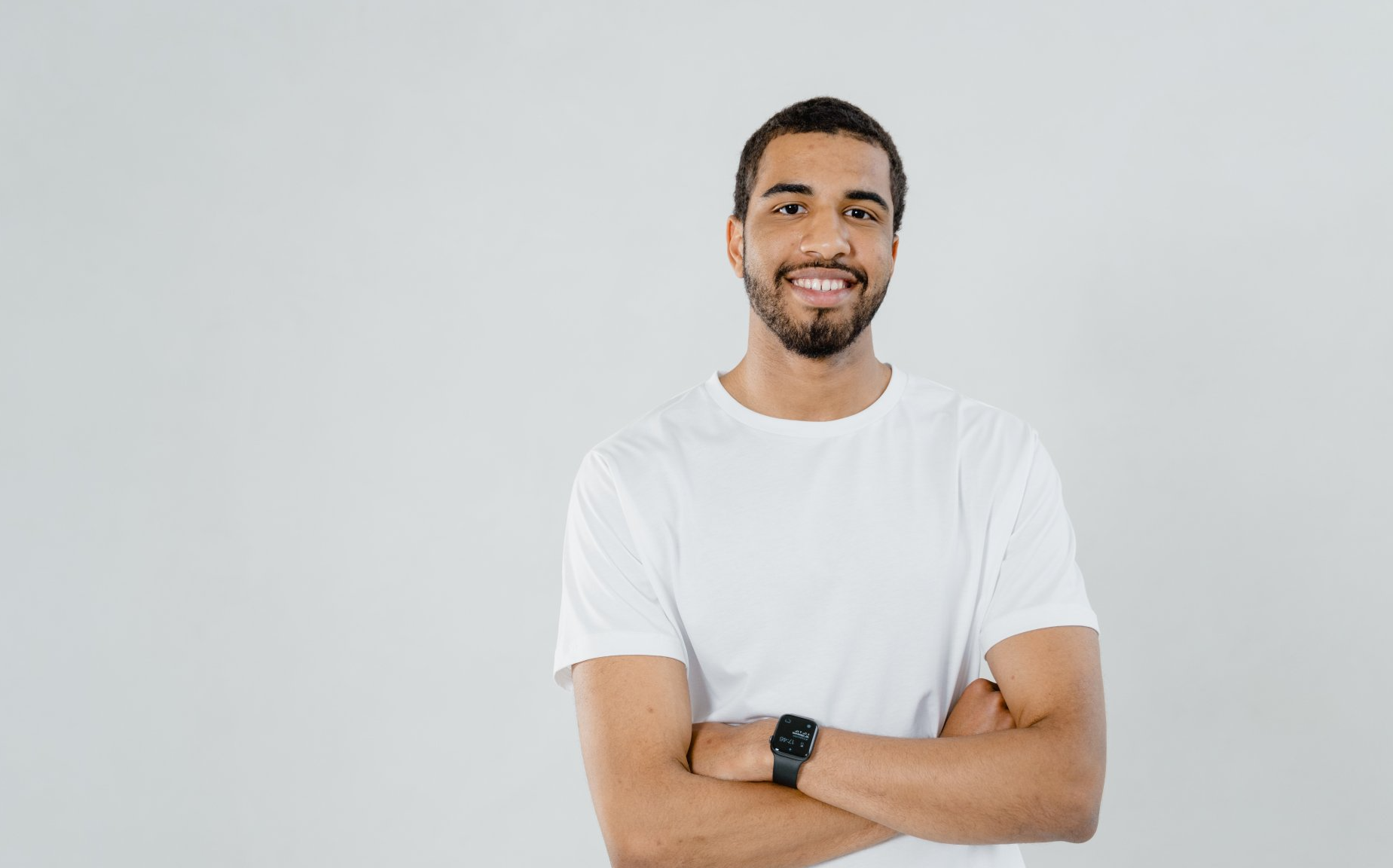 A man in a white t-shirt is standing with his arms crossed and smiling.