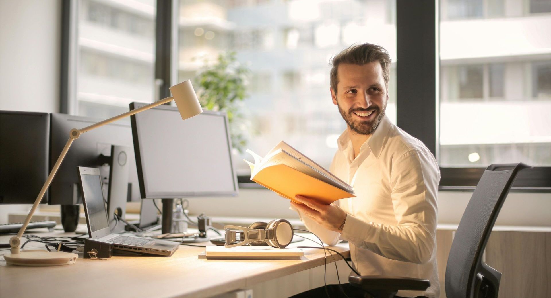A man is sitting at a desk in an office holding a folder.