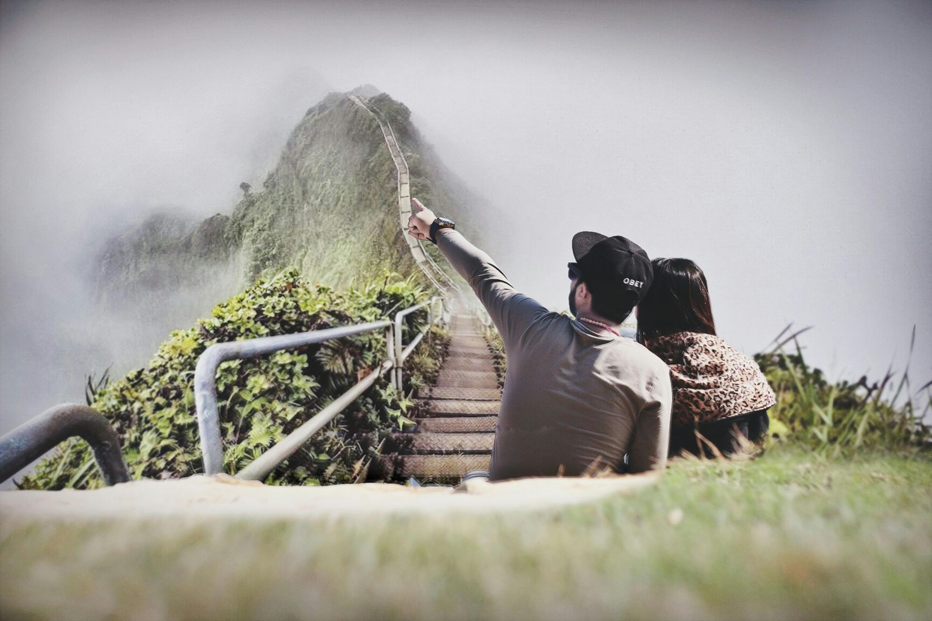 Couple pointing toward mountain peak obscured by fog.