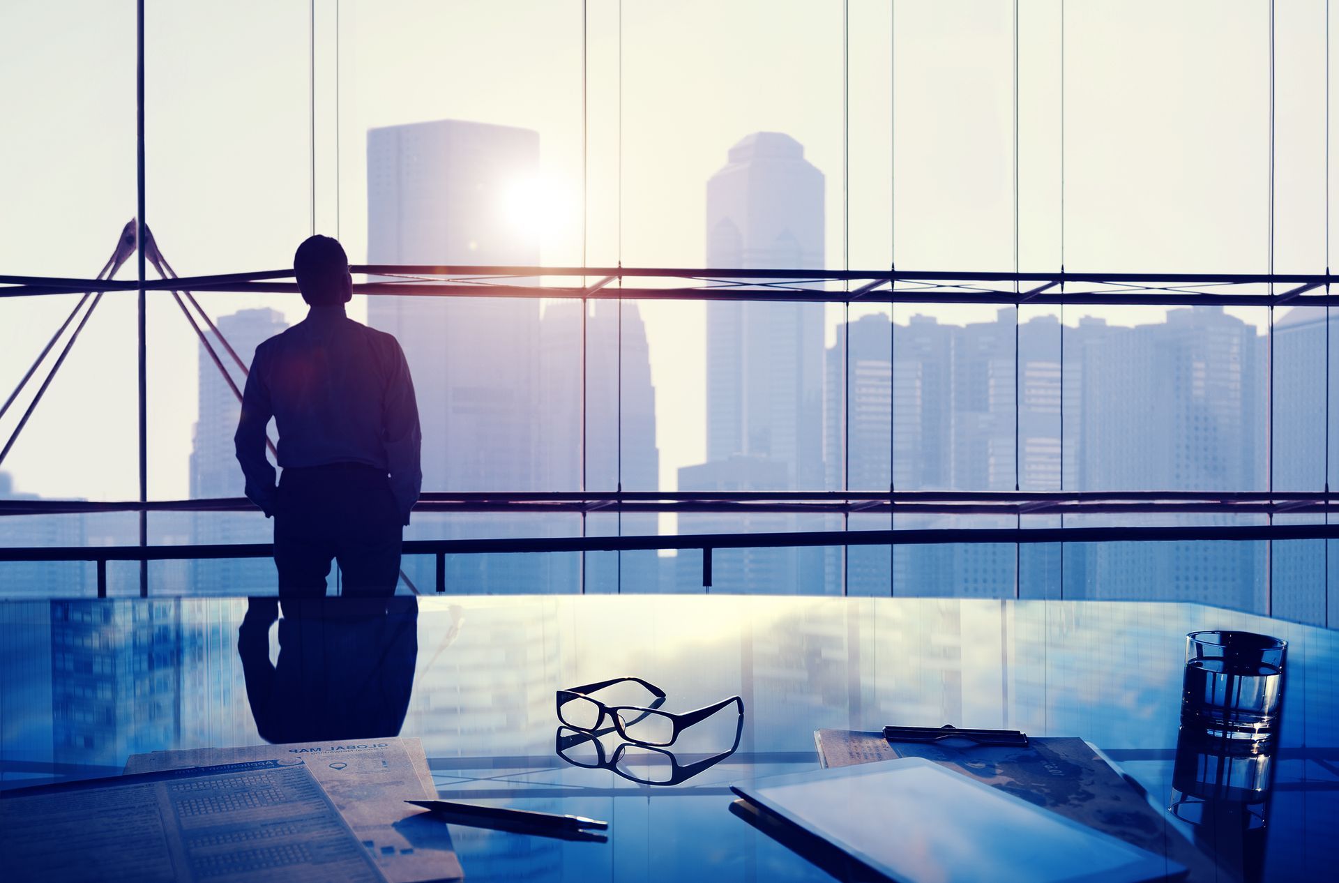 Silhouette of a person gazing out a window at a city skyline.