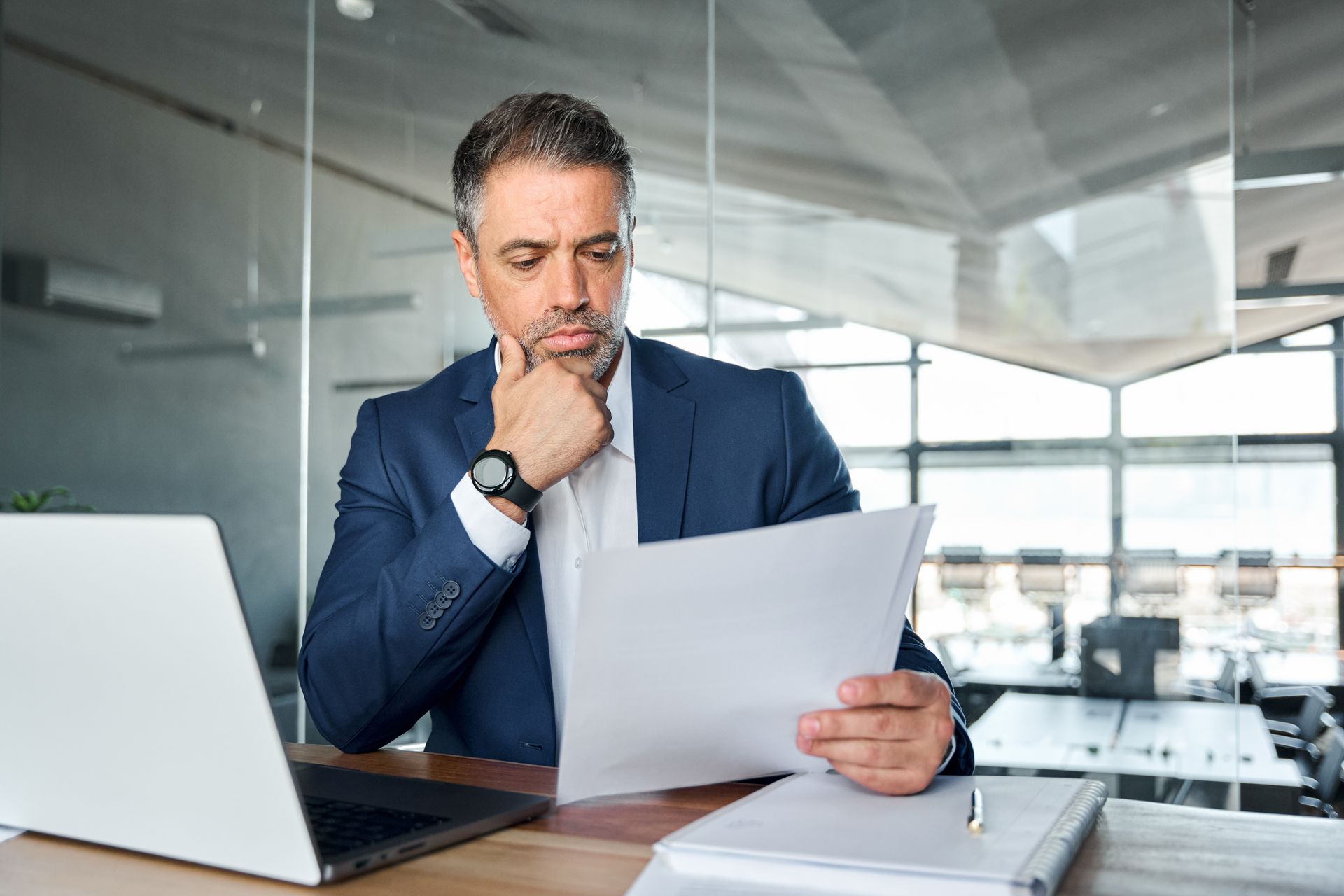 A man in a suit is sitting at a desk looking at a piece of paper.