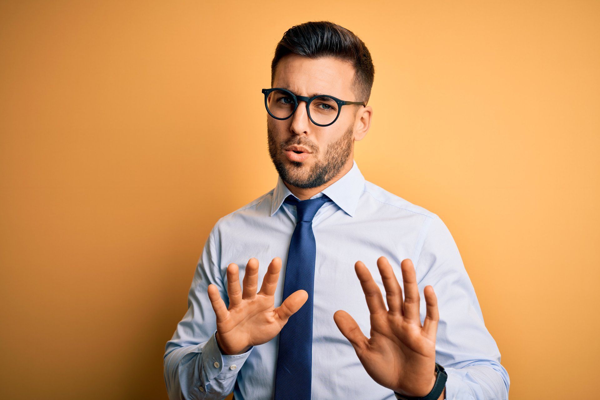 A man wearing glasses and a tie is making a stop sign with his hands.