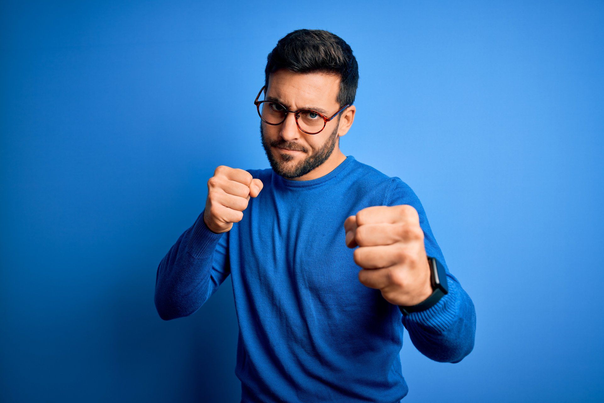 A man wearing glasses and a blue sweater is holding his fists up in the air.