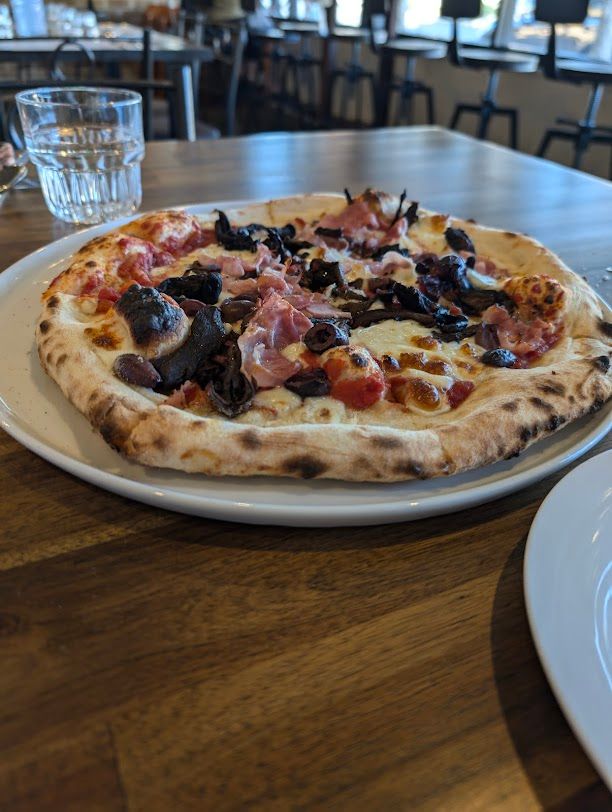 A Pizza Is Sitting On A White Plate On A Wooden Table — Mumbo's Pizza'n'Pasta In Lismore, NSW