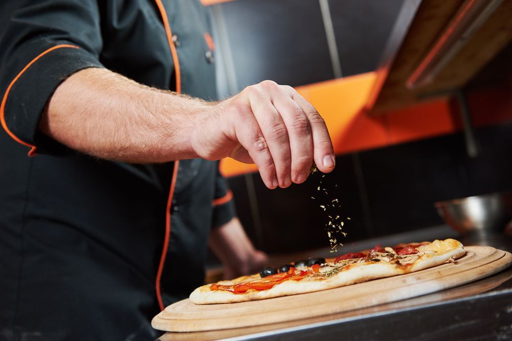 A Chef Is Sprinkling Seasoning On A Pizza — Mumbo's Pizza'n'Pasta In Lismore, NSW