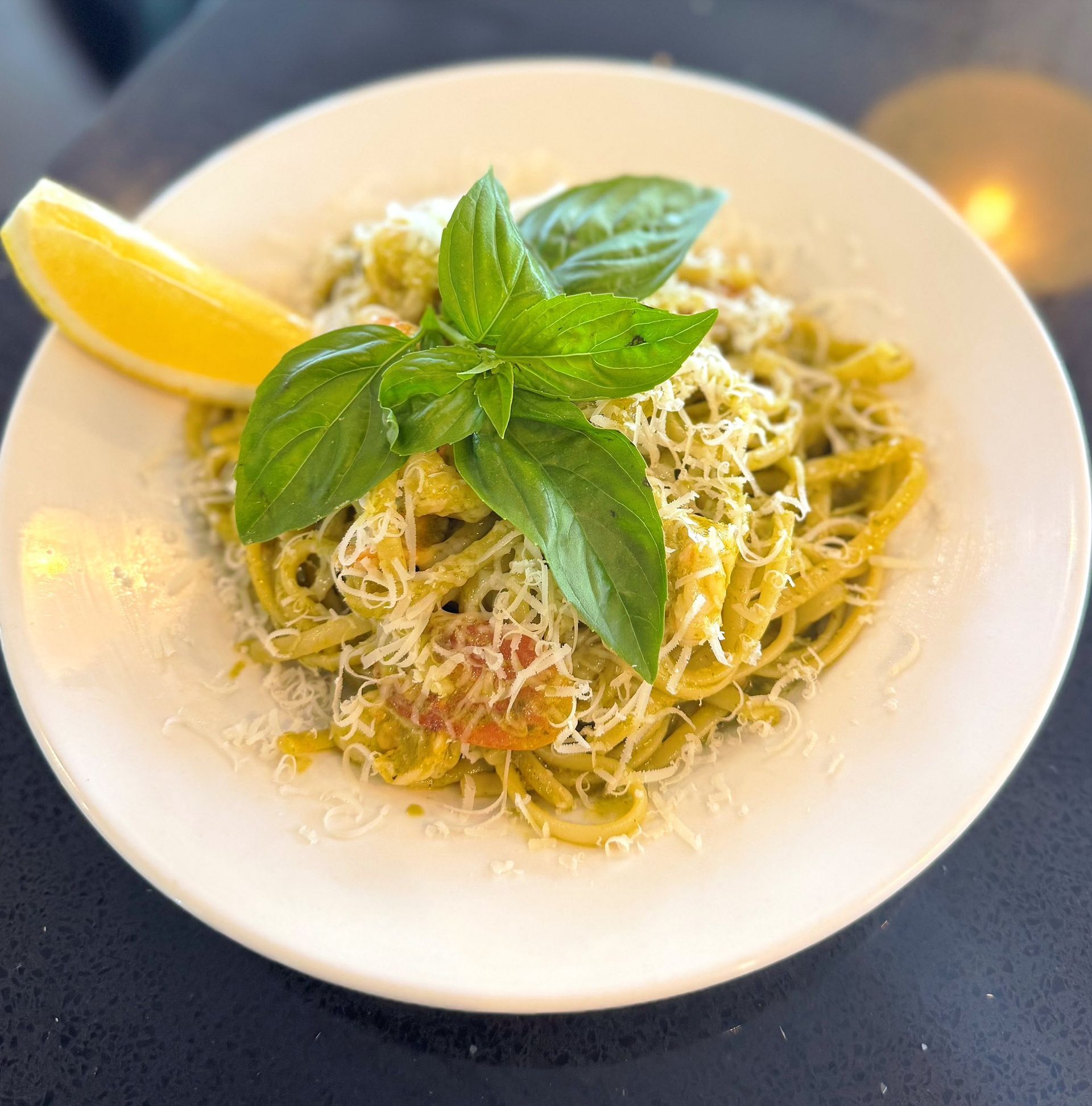A white plate topped with noodles , basil , cheese and a slice of lemon.