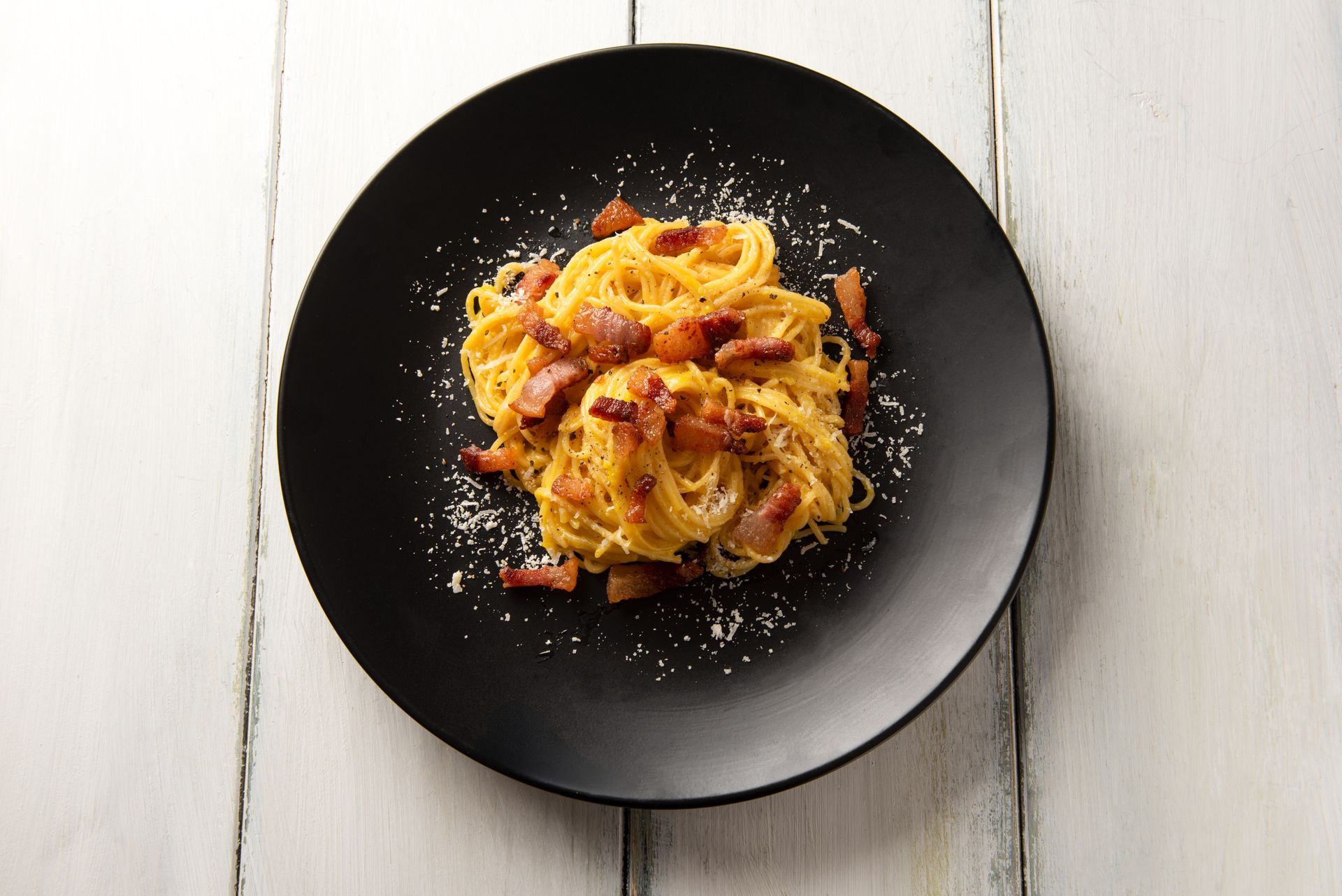 A Black Plate Topped With Spaghetti and Bacon on a Wooden Table — Mumbo's Pizza'n'Pasta In Lismore, NSW