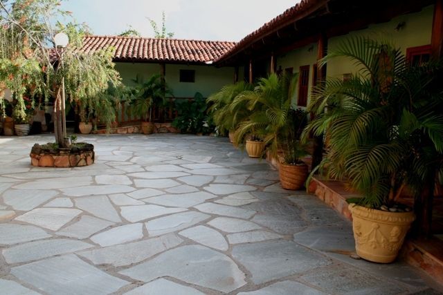 Pedra Lajão natural aplicada em pisos e caminhos externos, com grandes peças irregulares em tons de cinza, verde e bege integradas ao paisagismo tropical.