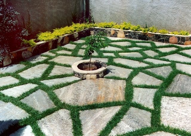 Pedra Lajão natural aplicada em pisos e caminhos externos, com grandes peças irregulares em tons de cinza, verde e bege integradas ao paisagismo tropical.