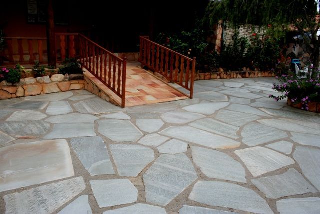 Pedra Lajão natural aplicada em pisos e caminhos externos, com grandes peças irregulares em tons de cinza, verde e bege integradas ao paisagismo tropical.