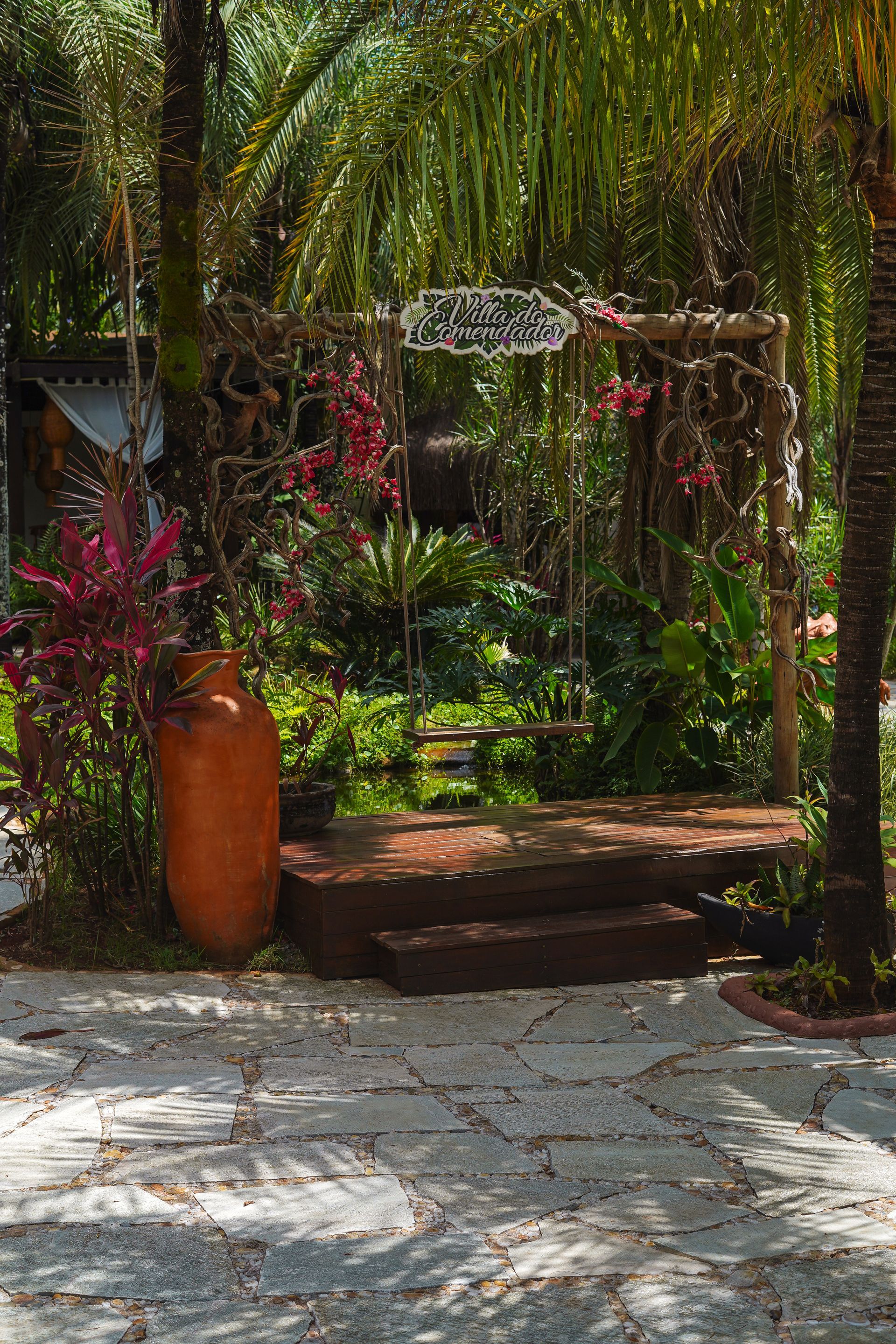 Pedra Lajão natural aplicada em pisos e caminhos externos, com grandes peças irregulares em tons de cinza, verde e bege integradas ao paisagismo tropical.