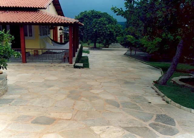 Pedra Lajão natural aplicada em pisos e caminhos externos, com grandes peças irregulares em tons de cinza, verde e bege integradas ao paisagismo tropical.
