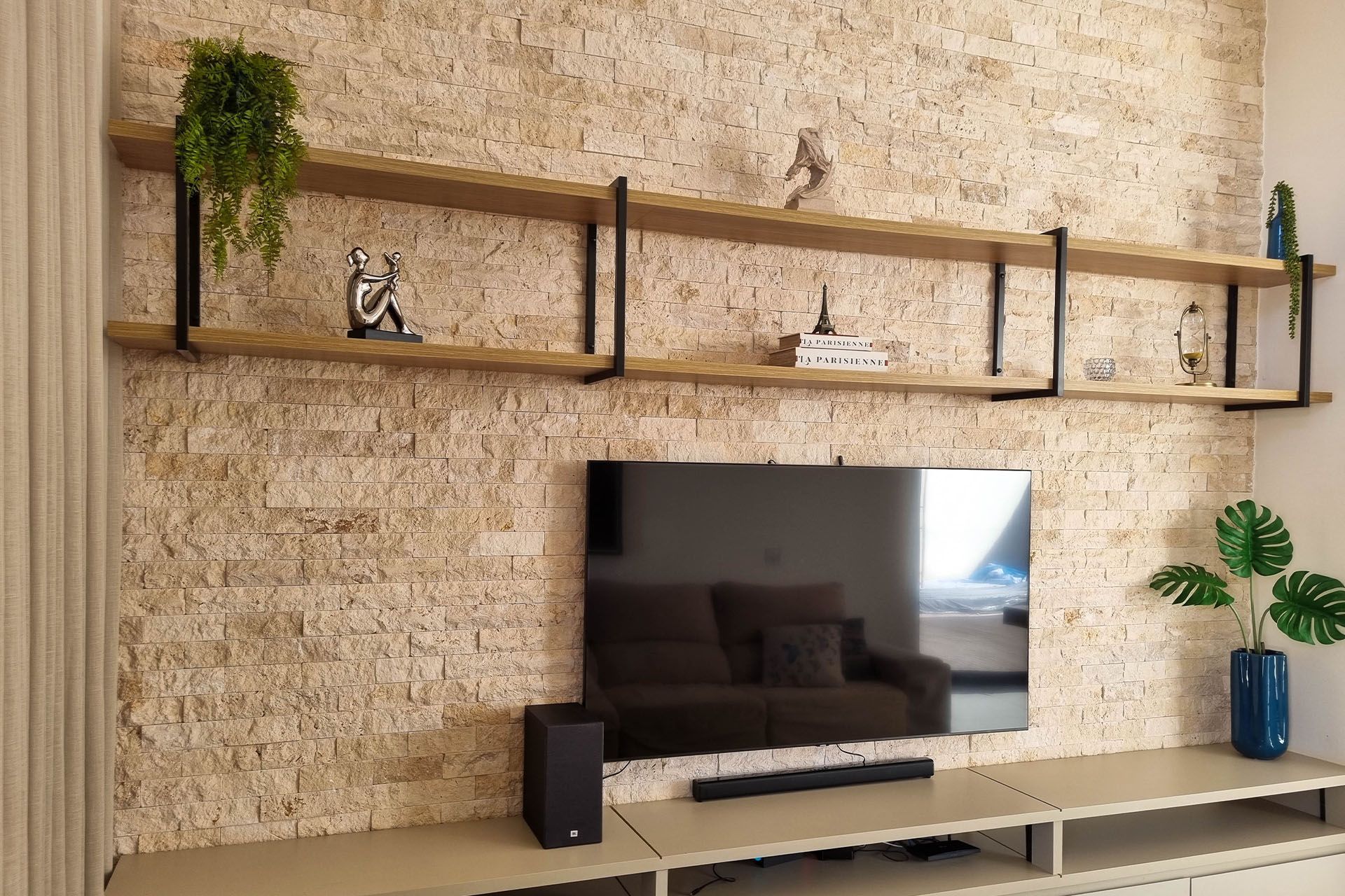 Sala de estar moderna com prateleiras fixadas na parede, TV e uma parede de travertino nacional de destaque com textura bege.