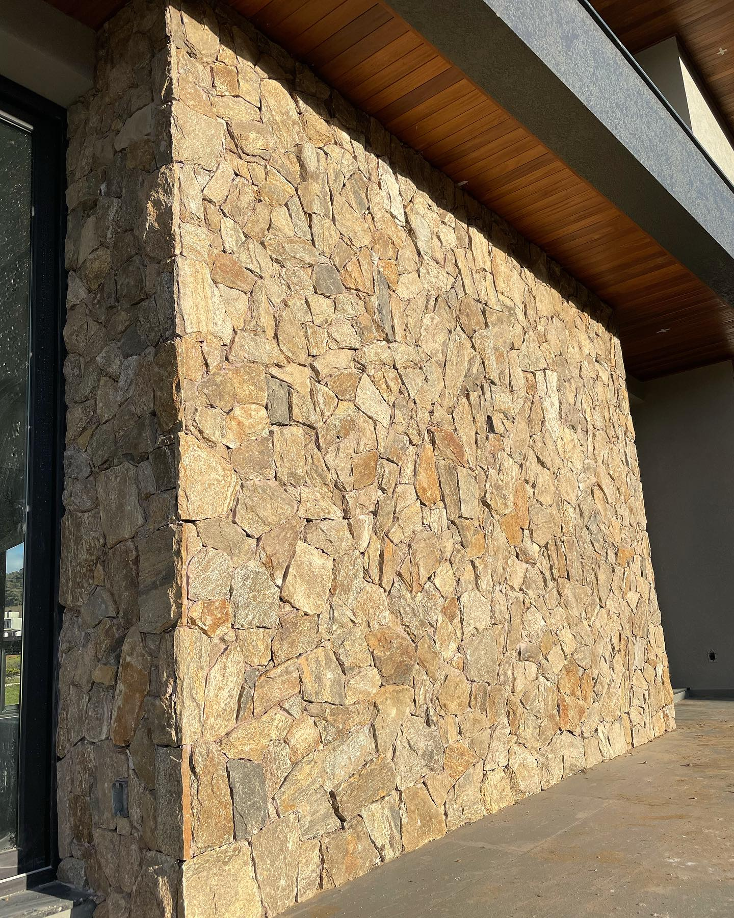 Pedra Amazon natural aplicada em fachadas, paredes e ambientes internos, com variações de tons terrosos, dourados e acinzentados.