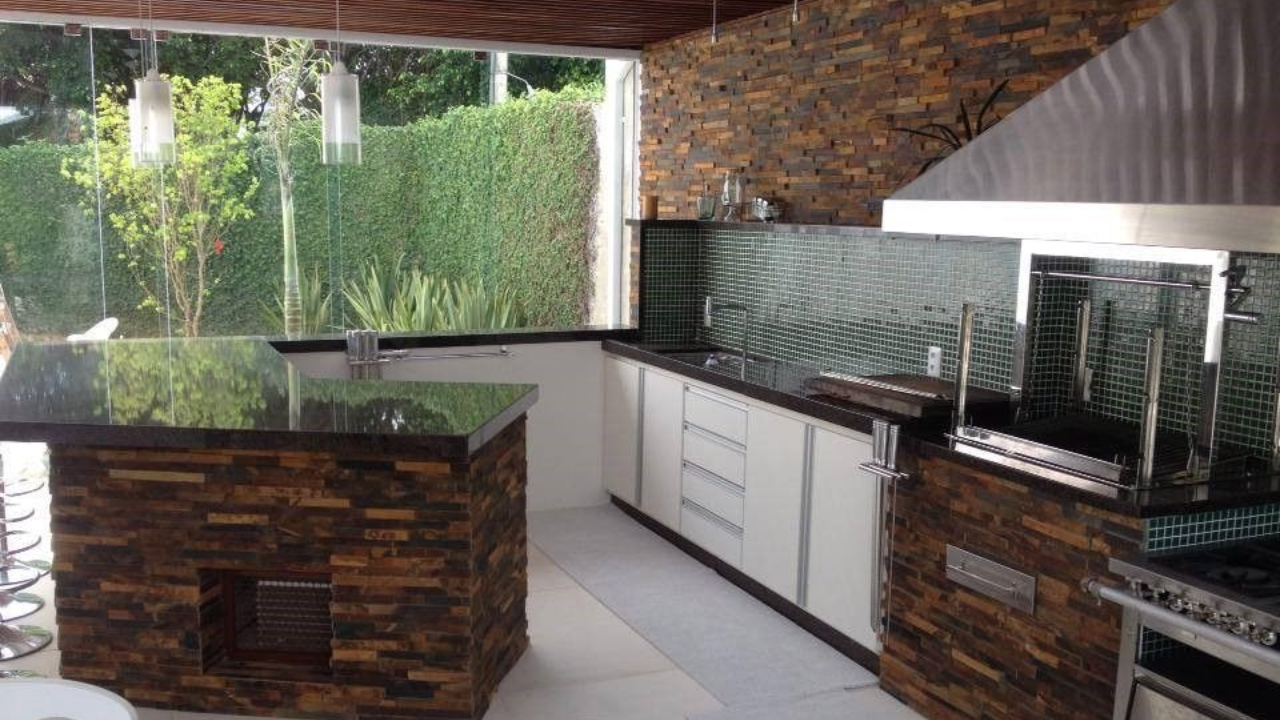 Área gourmet com revestimento de pedra natural, espaço para refeições e integração com o jardim.