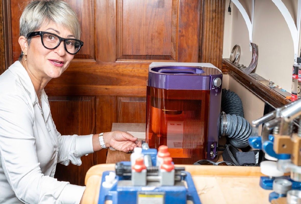 Woman with short gray hair and glasses working beside a clear container in a wooden kitchen setting