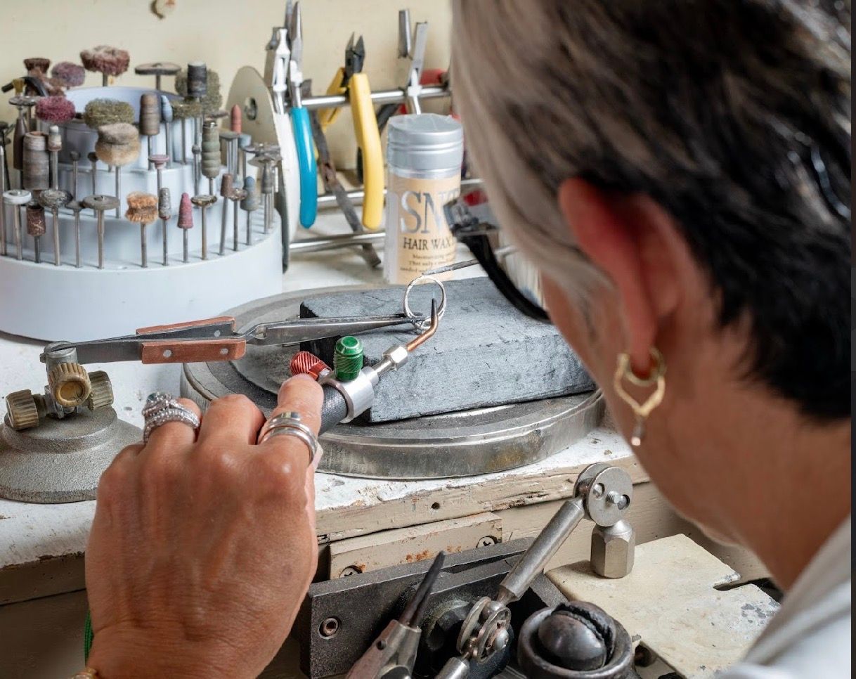 Person using a jeweler's tool at a workbench, with tools and small parts in the background
