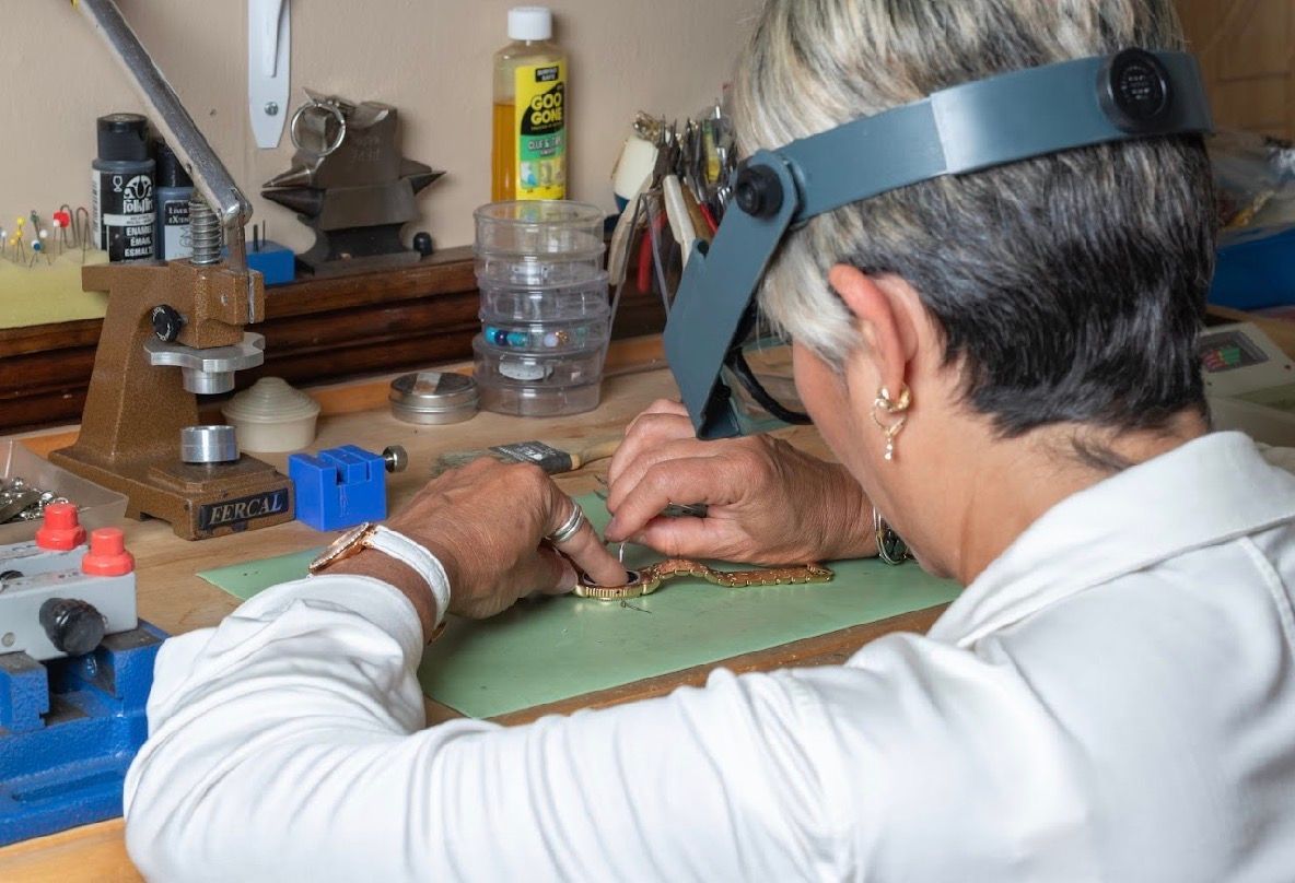 Person wearing a headband loupe works with tools at a jewelry bench in a workshop.