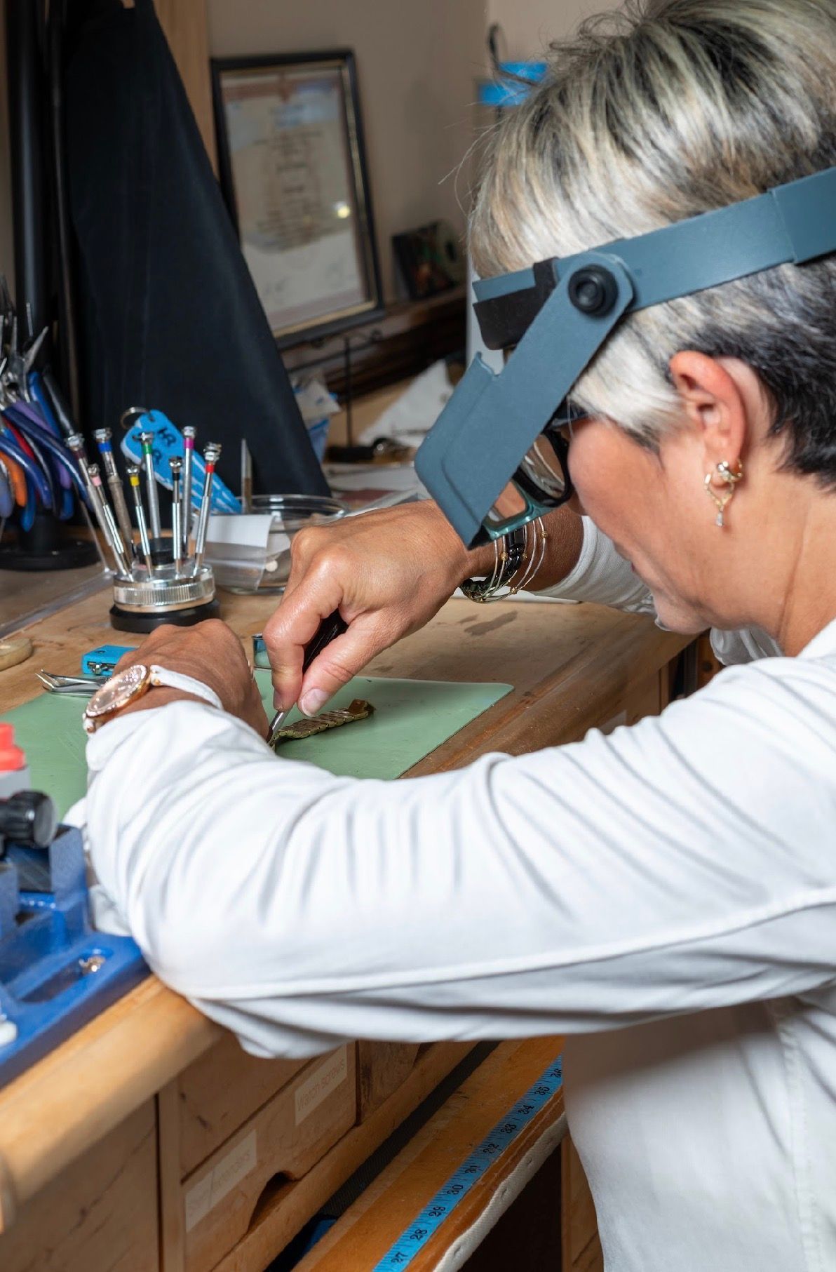 Person works at a desk using a magnifying headband to handle a small object with tools.